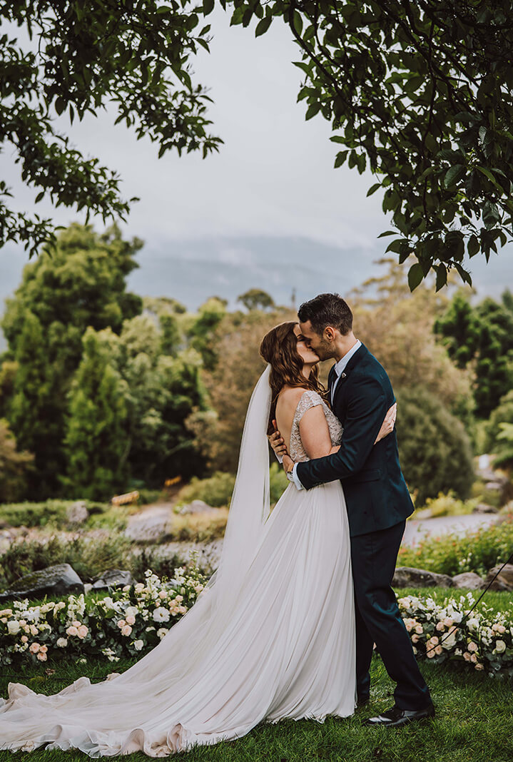 Bride and groom kiss with views of lush gardens and mountains behind them