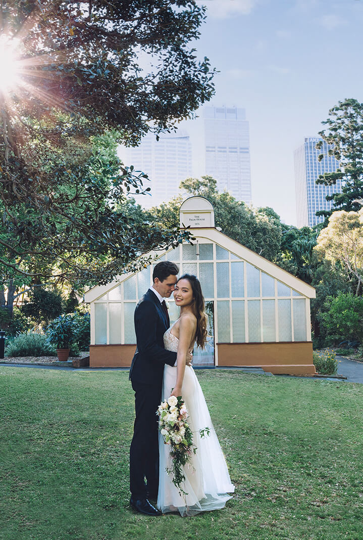 Bride and groom in Garden with historic retro greenhouse wedding venue in background