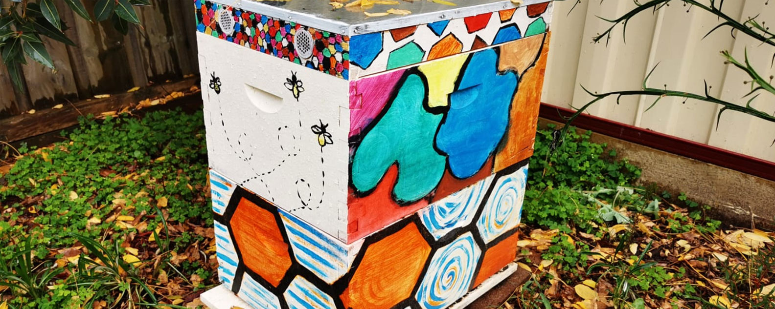 A colourfully painted bee hive in a garden with dead leaves