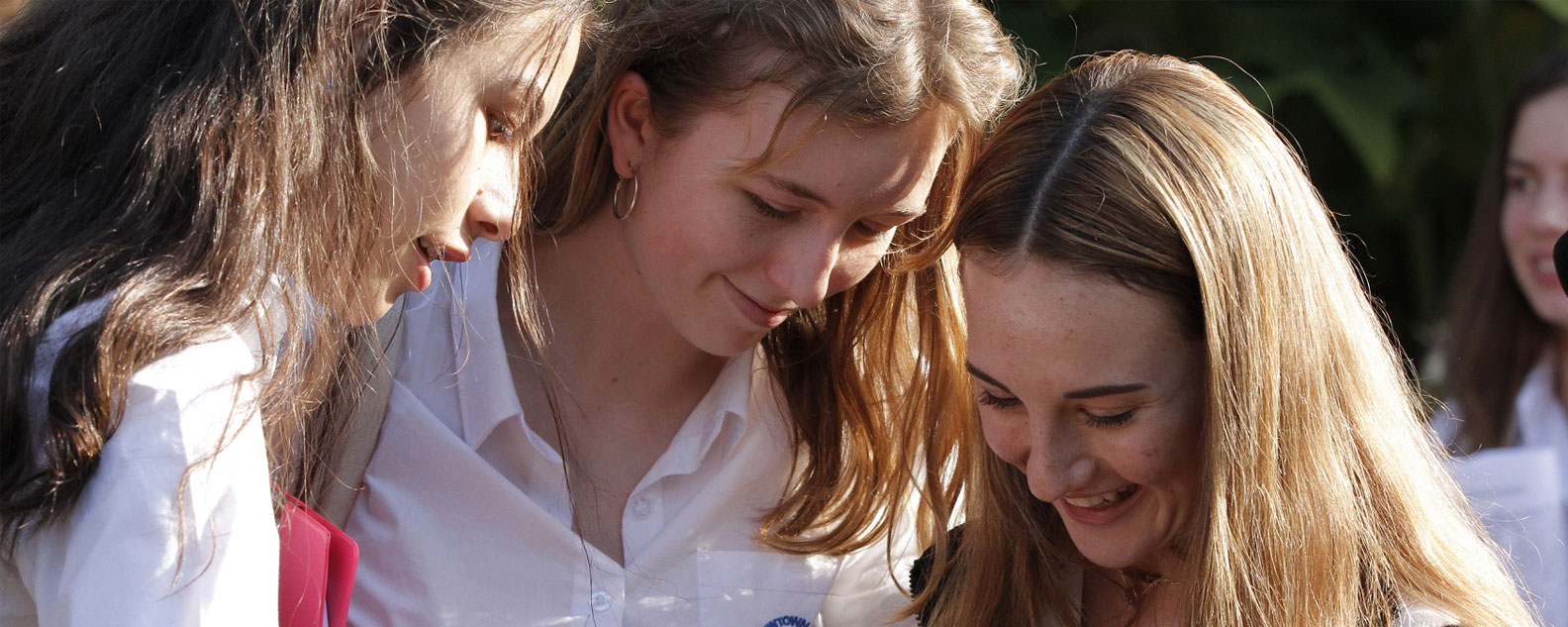 Three senior students smiling and looking down at something.