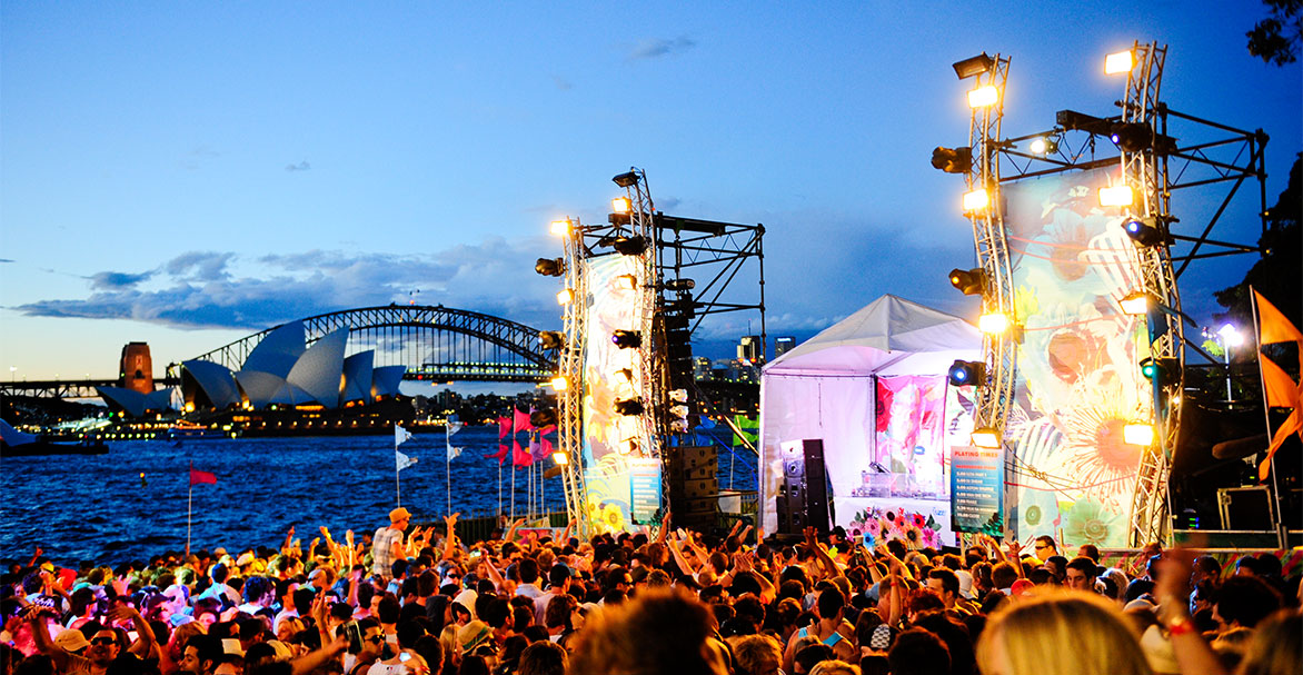 A crowd at a festival and a stage in The Domain with Sydney Harbour in the background
