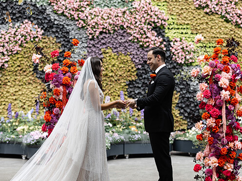 Bride and groom in front of colourful greenery and floral arrangements. Credit: Salt Atelier Photography