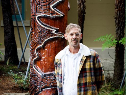 Darren Charlwood, a Wiradjuri artist, stands next to his Welcome to Country Sculpture at the Botanic Garden of Sydney.