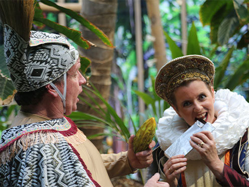 A man and woman in costume eating chocolate surrounded by plants