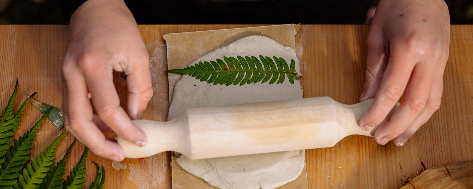 A child rolling out clay with a fern leaf on it