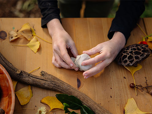 A child rolling out clay with natural materials scattered on the bench