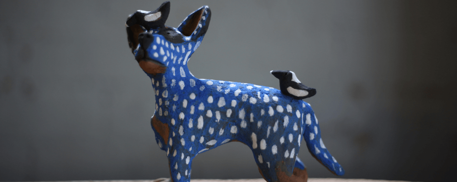 Blue ceramic dog sculpture with white spots and black and white bird sitting on back