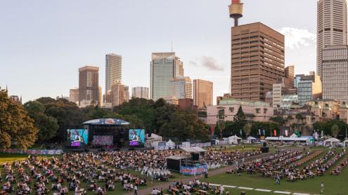 A socially-distanced, seated crowd in the Domain watching a concert with Sydney city skyline in the background