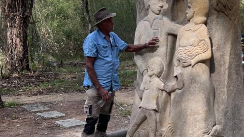 First Nations man puts his hand to the sculpture of a family together