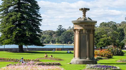 Stone monument with flower beds surrounding it and harbour in the background