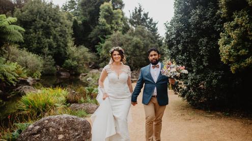 Bride and groom walk along sandy path with dense gardens around them