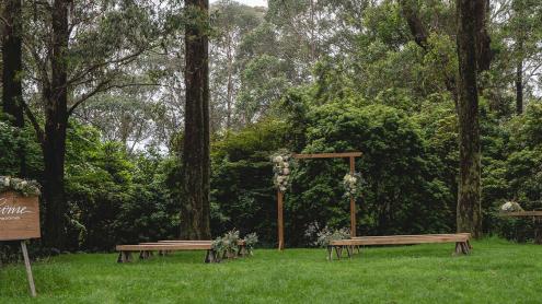 Lawn surrounded by tall eucalyptus trees, with rustic benches, flower arbour and a welcome sign ready for a wedding