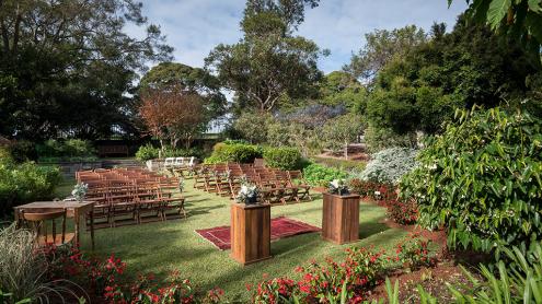 Lawn surrounded by lush garden, with chairs set up for a wedding ceremony