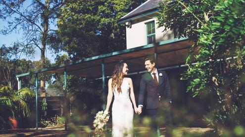 Bride and groom hold hands outside a charming, cream-coloured house