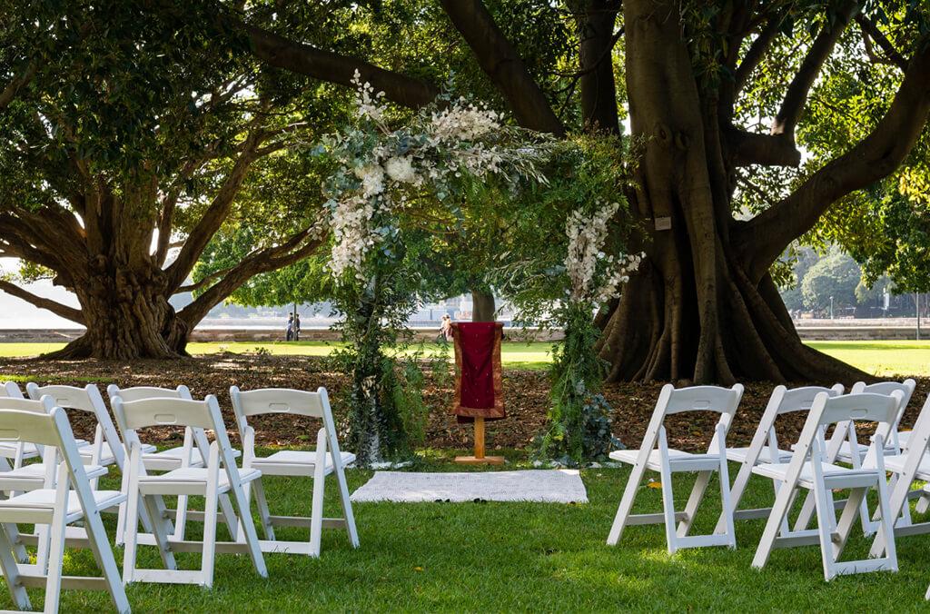 White chairs and wedding arch under fig trees