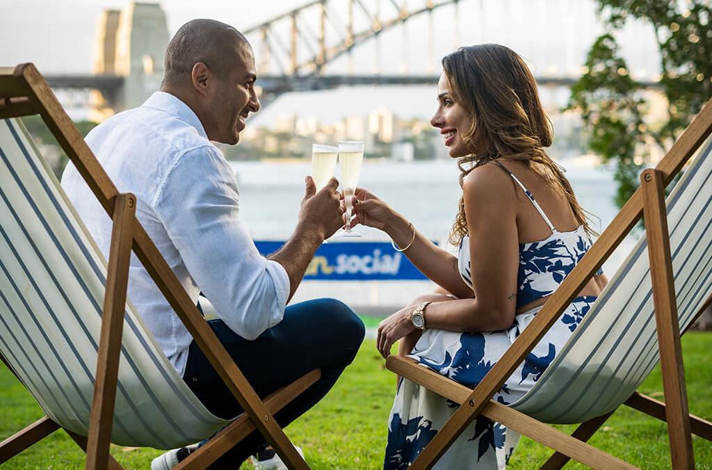 Couple on deck chairs, with champagne, overlooking Sydney Harbour