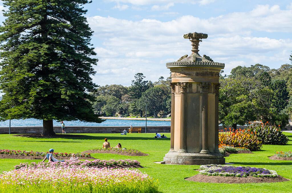 Stone monument with flower beds surrounding it and harbour in the background