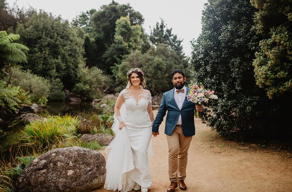 Bride and groom walk along sandy path with dense gardens around them