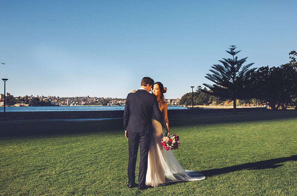 Bride and groom pose on lawn overlooking Sydney Harbour
