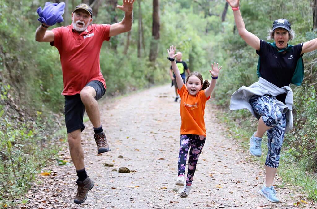 A family jumping with their hands up whilst participating in the parkrun