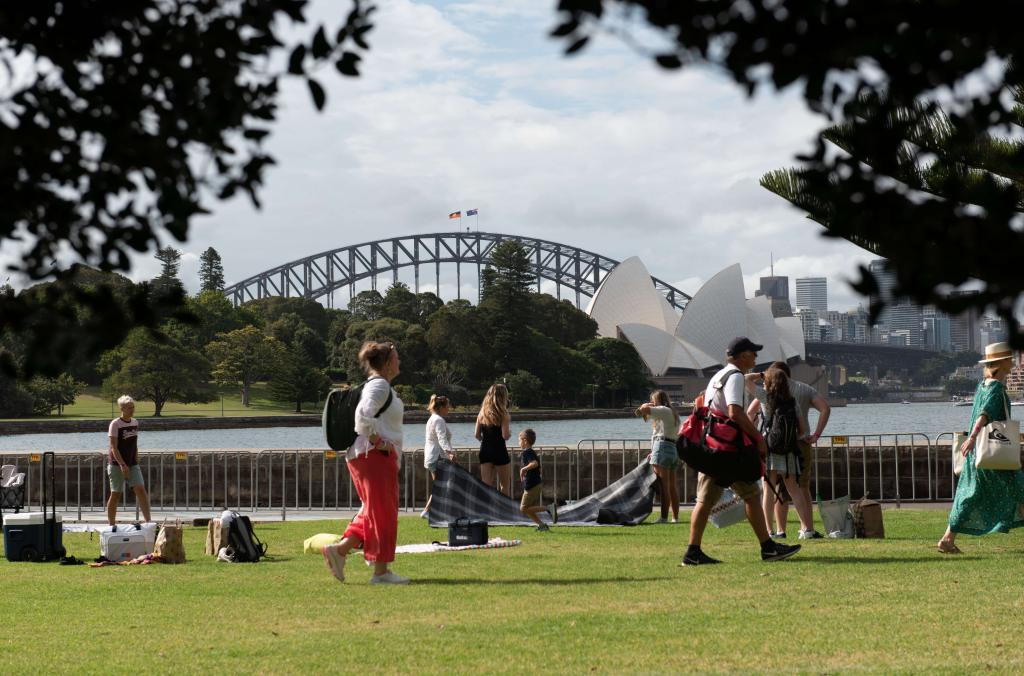 People walking across the lawn in front of views of the Sydney Harbour Bride and Opera House.