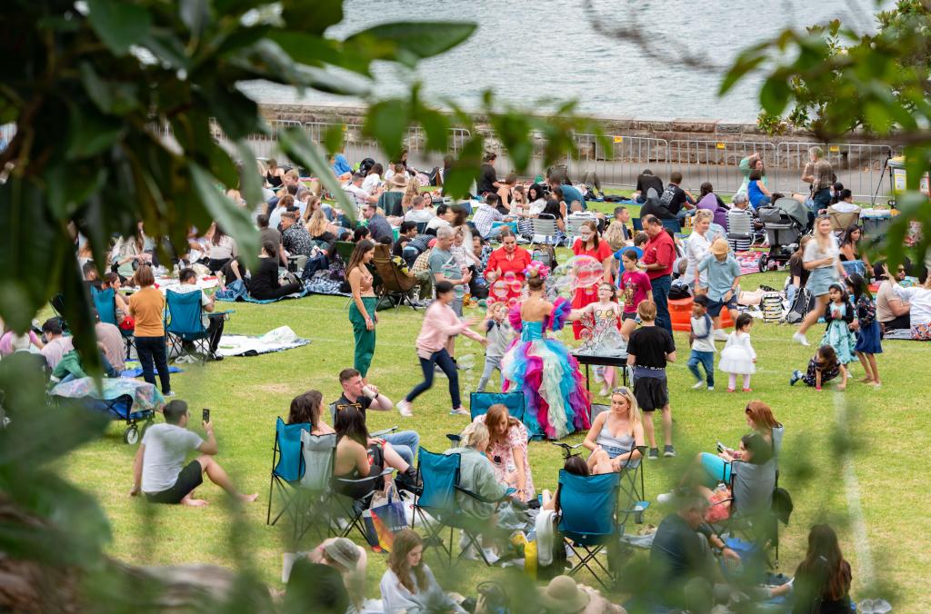 People gathered on the lawn, many surrounding an entertainer dressed in colour blowing bubbles.