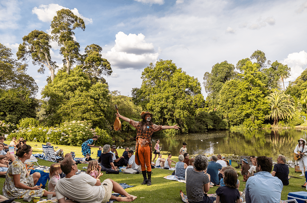 People watching the Wind in the Willows performance on the lawn with a pond in the distance